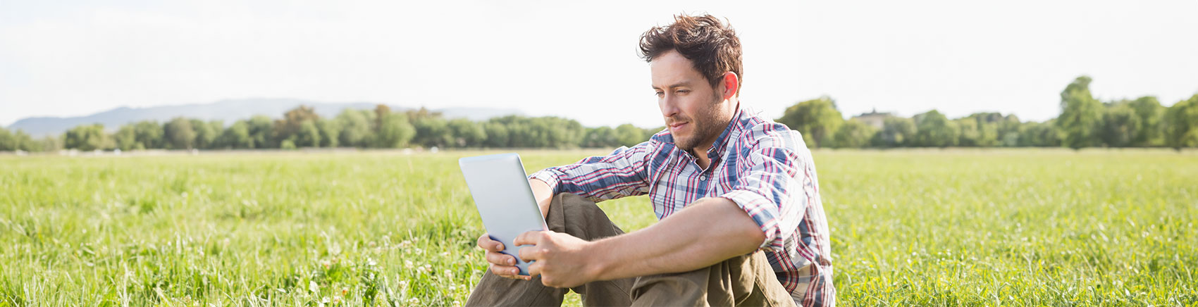 ETF-Portfolio Strategie Junger Mann sitzt auf einer Wiese und schaut in sein Tablet