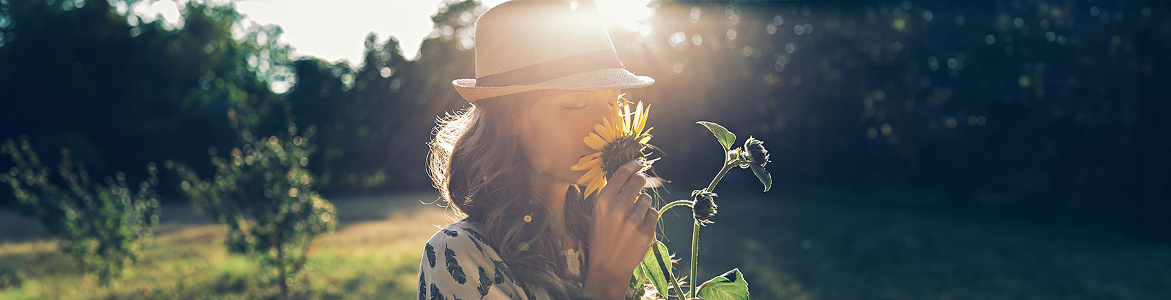 Nachhaltig investieren Frau mit Hut riecht an einer Sonnenblume