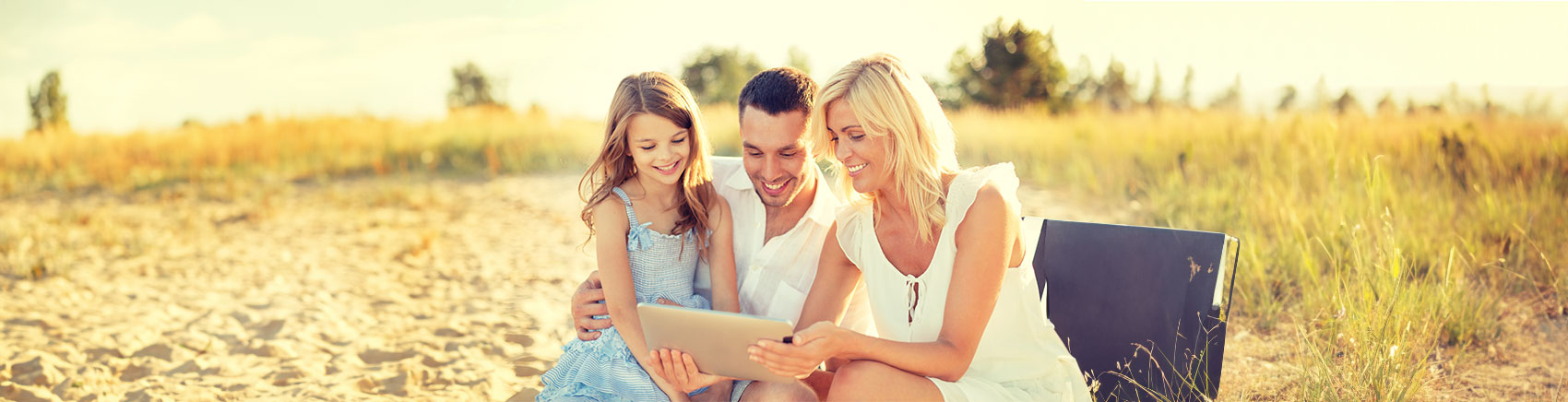 Depot für Kinder Familie sitzt am Strand und schaut gemeinsam in ein Tablet